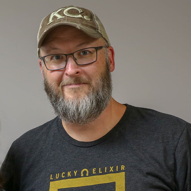Man wearing a cap and 'Lucky Elixir' t-shirt against a plain background