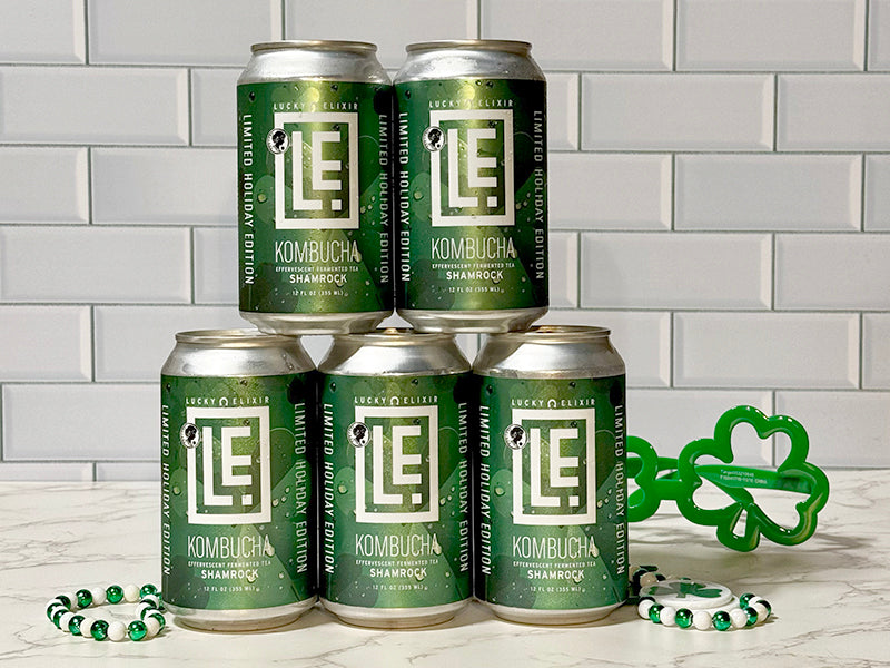 Five cans of LE Kombucha on a white surface with a gray tiled wall background