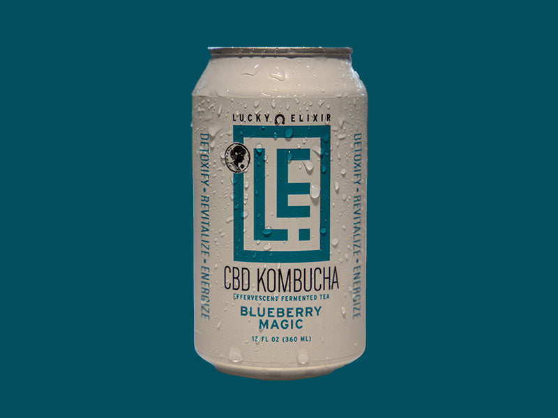 A can of Lucky Elixir CBD Kombucha with the flavor Blueberry Magic. The can is white with a geometric pattern and blue text.