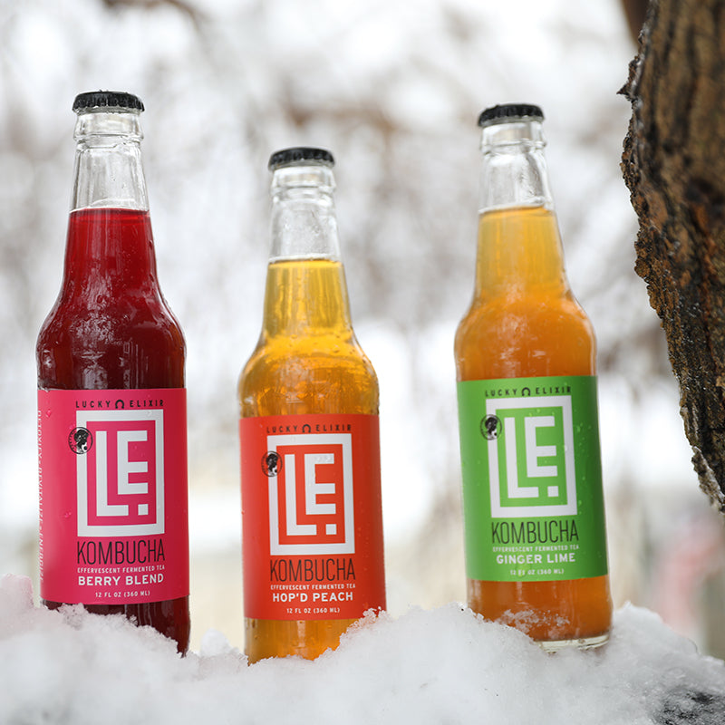 Three bottles of Lucky Elixir Kombucha in different flavors standing in the snow.
