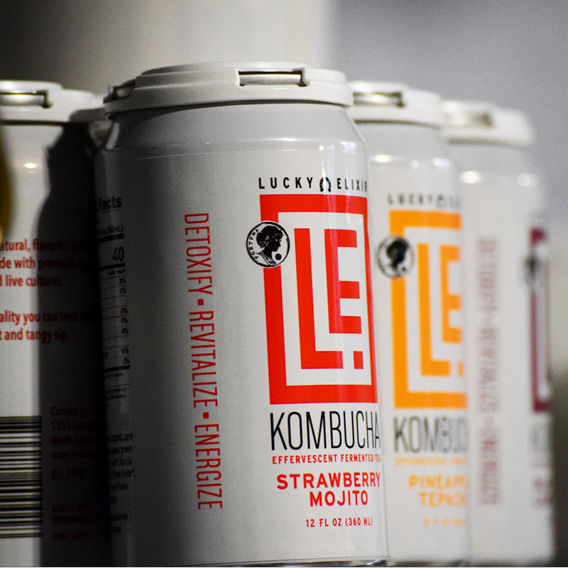 Lucky Elixir kombucha cans with visible branding and product names.