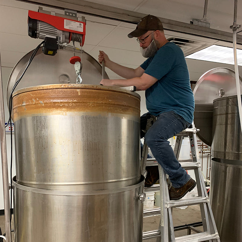Person working on a large metal tank with a ladder in an industrial setting